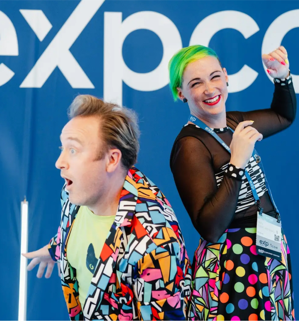 Two people dancing in front of the eXp con sign.